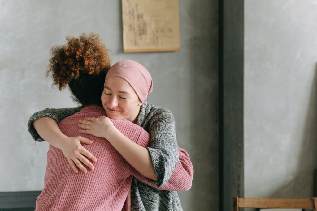pexels-thirdman-7659454 Two women hug. One is wearing a pink sweater; the other is wearing a pink scarf over her head. They appear to be comforting each other.